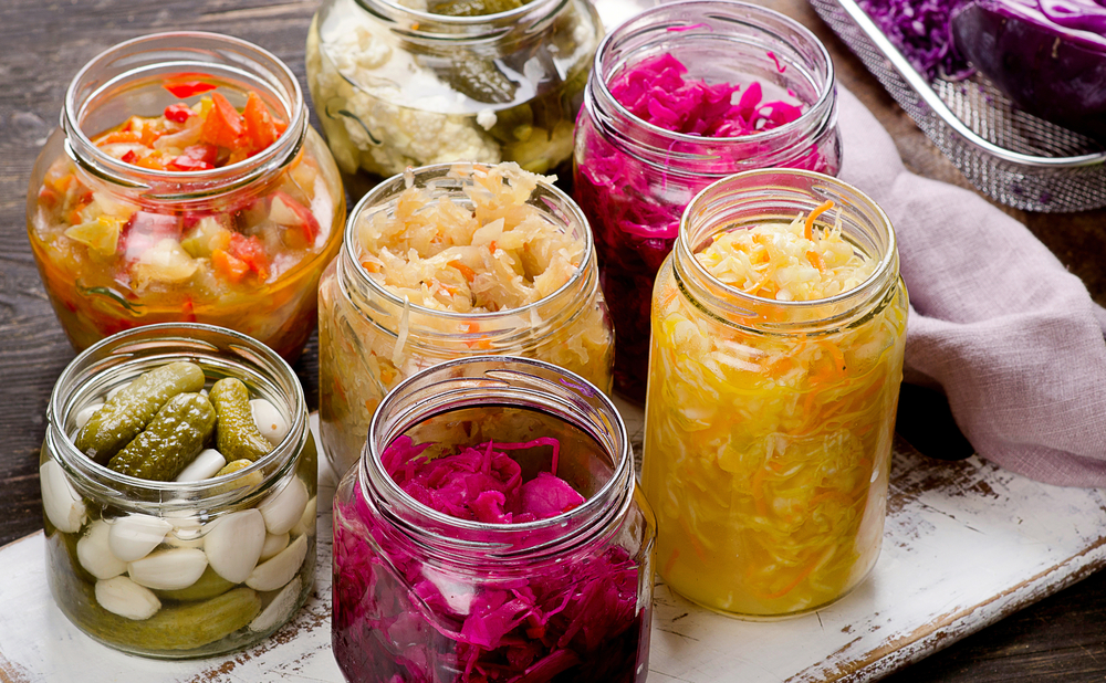 Seis frascos de vidrio que contienen alimentos probióticos como el chucrut que cuidan la flora intestinal