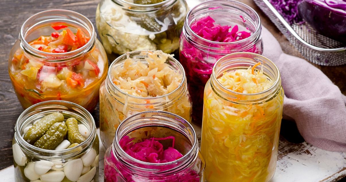 Seis frascos de vidrio sin tapa que dejan ver alimentos fermentados fuente de probioticos como el chucrut