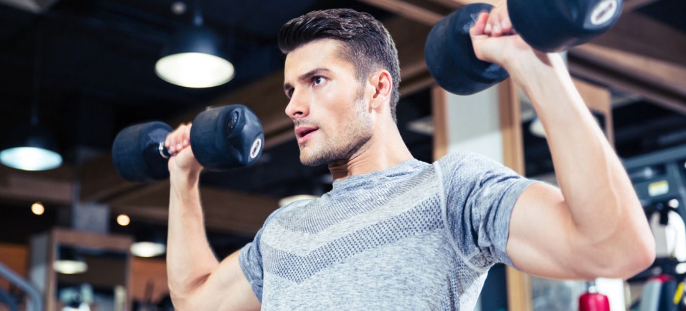 Hombre joven moviendo pesas en el gimnasio para aumentar su índice de masa muscular
